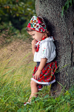 en liten jente står ettertenksomt lent mot et tre