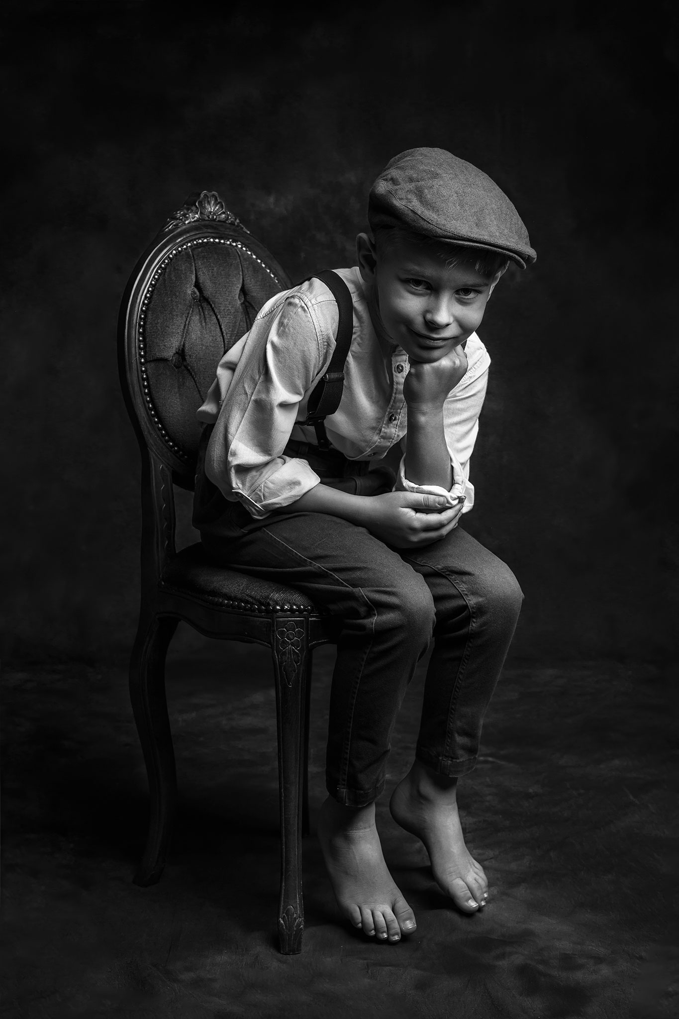 smilende liten gutt sitter på en stol i gamle klær og en beret på hodet