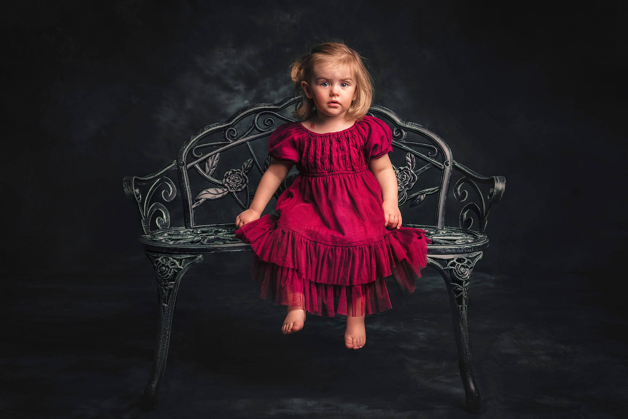 en liten jente i en fin kjole sitter smilende på en benk