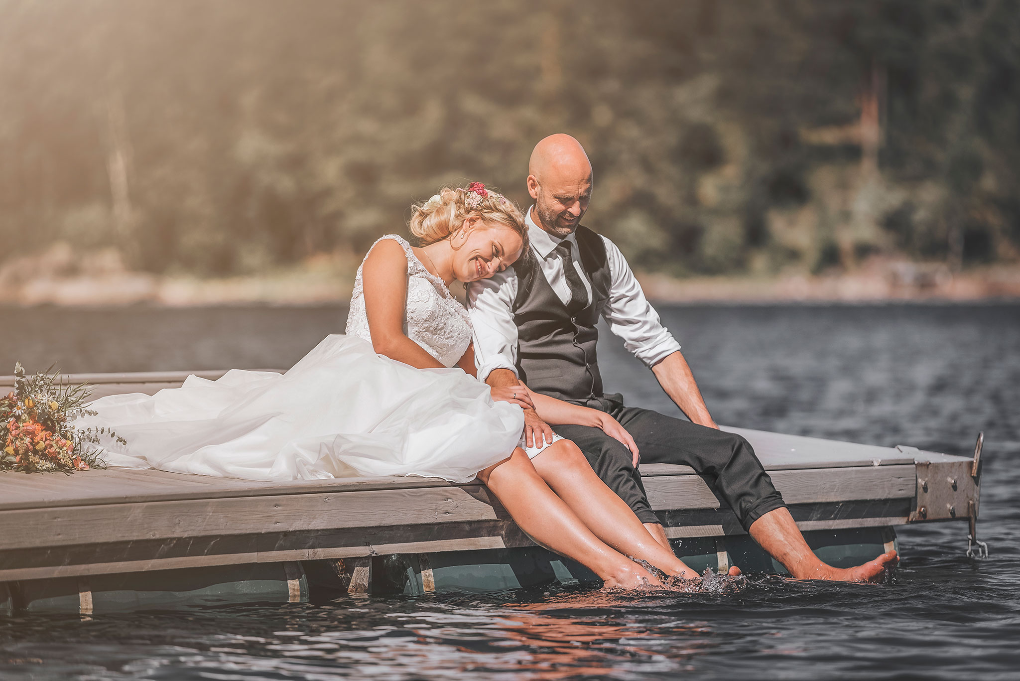 brudepar klemmer mens de sitter på brygga og legger føttene i vannet