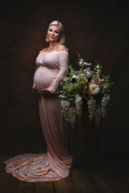 en elegant kledd gravid kvinne poserer i studio ved siden av vakre blomster