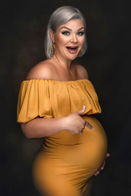 en smilende gravid kvinne poserer til gravidbilder i en gul kjole