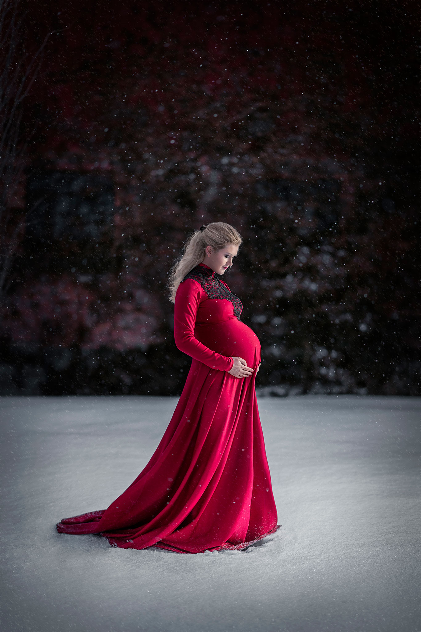 gravid kvinne i en lang rød kjole står på snø
