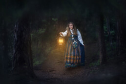 en jente i bunaden går gjennom den mørke skogen med lykt