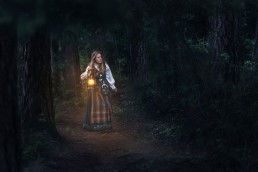 en jente i bunaden går gjennom den mørke skogen med lykt